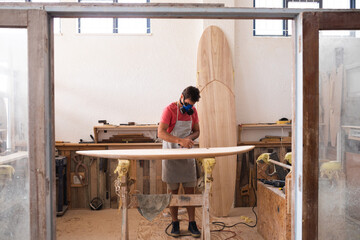 Caucasian male surfboard maker, wearing a preparing to polishing a surfboard