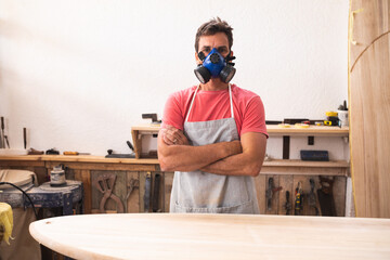 Caucasian male surfboard maker wearing a protective apron and a mask, looking at camera