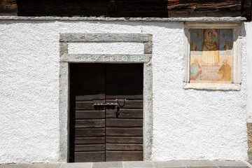 Obraz na płótnie Canvas Canza (VCO), Italy - June 21, 2020: An old wooden door and a religius paint at Canza village, Formazza Valley, Ossola Valley, VCO, Piedmont, Italy