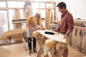 Two Caucasian male surfboard makers discussing the project and using a tablet computer