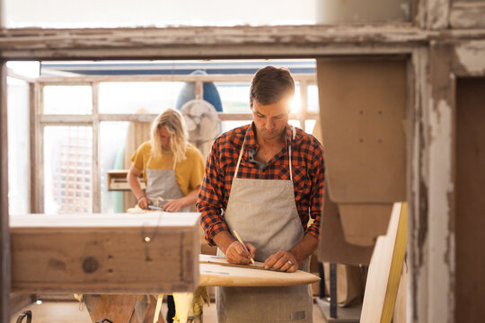 Two Caucasian male surfboard makers making a wooden surfboard together and inspecting it 