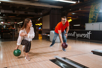 Fototapeta premium A beautiful loving caucasian couple throwing balls on the bowling alley. Boyfriend and girlfriend at the bowling club