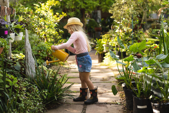 A Caucasian girl watering plants with watering can in a sunny garden
