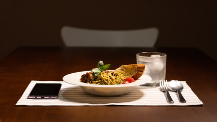 A neat setup with dramatic lighting of dinner on wooden table with a plate of spaghetti, spoon and...