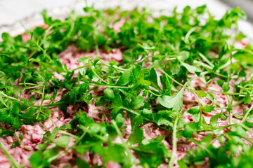 A large crystal cut-glass bowl with puff salad herring under a fur coat, a Russian dish with boiled beetroot and mayonnaise, green leaves of watercress on top. White textured stone background
