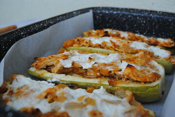 Stuffed Zucchini Boats with chicken, carrots, and onions, poured with sour cream in a metal pan.