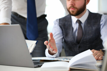 Stylish young man sitting at the table with modern notebook while working with male colleague in office