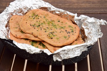 Whole wheat sesame garlic naan bread in aluminum foil on wooden table.
