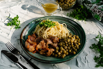 A hearty meal on the table, spaghetti with fried pork chunks, green canned peas and watercress grass. Next to the sauce and a bowl of peas. Green interesting plate