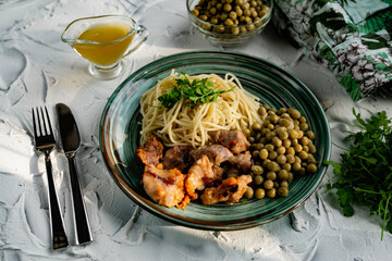 A hearty meal on the table, spaghetti with fried pork chunks, green canned peas and watercress grass. Next to the sauce and a bowl of peas. Green interesting plate