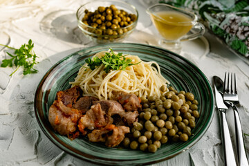 A hearty meal on the table, spaghetti with fried pork chunks, green canned peas and watercress grass. Next to the sauce and a bowl of peas. Green interesting plate