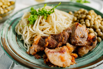 A hearty meal on the table, spaghetti with fried pork chunks, green canned peas and watercress grass. Next to the sauce and a bowl of peas. Green interesting plate