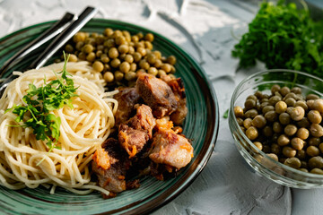 A hearty meal on the table, spaghetti with fried pork chunks, green canned peas and watercress grass. Next to the sauce and a bowl of peas. Green interesting plate