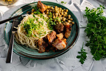 A hearty meal on the table, spaghetti with fried pork chunks, green canned peas and watercress grass. Next to the sauce and a bowl of peas. Green interesting plate