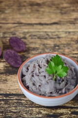 Vitelotte mashed purple potato in a bowl on wooden background garnish with parsley.