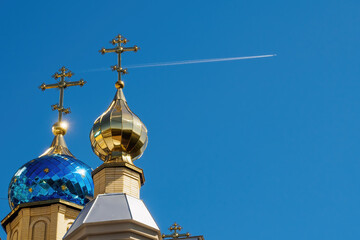 Domes of the temple with crosses against blue sky and flying plane with white trace. Orthodox church and flying airplane