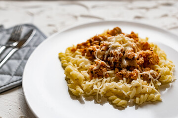 A simple dish on a white plate with boiled pasta in the form of spirals and meat Bolognese sauce in tomato paste, a hot dish with melted cheese.
