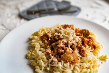 A simple dish on a white plate with boiled pasta in the form of spirals and meat Bolognese sauce in tomato paste, a hot dish with melted cheese.