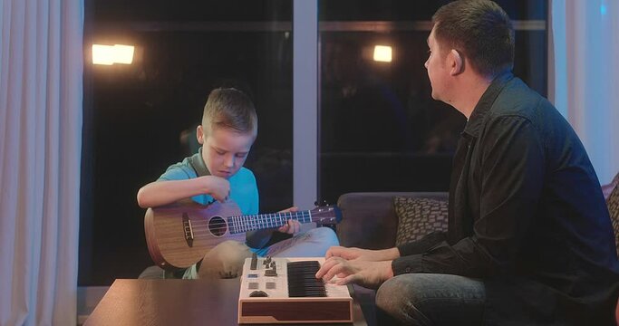 Father and son play guitar and piano at home. Dad teaches child to play musical instruments. Music hobby, Create, learning own songs. SHARE THE LOVE, play our game. 4K video.