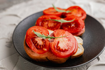 Three sandwiches with fresh and bright red tomatoes and smoked sausage, decorated with a leaf of green arugula on a matte black plate and a white stone background