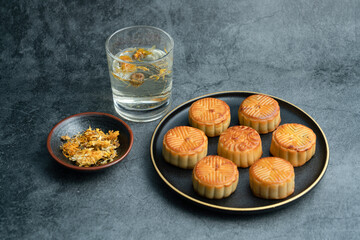 Moon cakes for the Mid-Autumn Festival are placed on a black plate with gold trim.
A plate of moon cake and a cup of chrysanthemum tea.