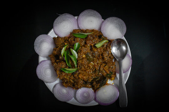 South Indian cuisine Kerala Style Beef fry / roast. Traditional style meat roast. Garnished with onion slices and curry leaves. Black background. Selective focus photograph.