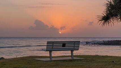 Fototapeta na wymiar A bench remains empty as the sun rises over the Coral Sea