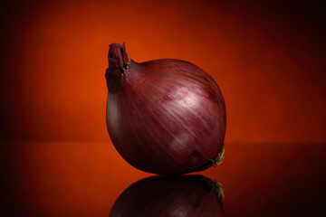 One red onion on a black and orange background with a reflection on the table
