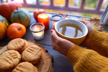 Close up of cup of tea with mint in female hand. Homemade peanut cookies, pumpkin and autumn yellow leaves on wooden background