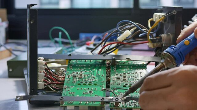 Electronic technician is soldering the electric wires to the motherboard of an electronic device.