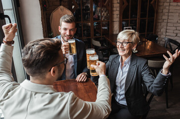 Senior businesswoman sitting with her younger male colleagues at cafe taking a brake and drinking beer.
