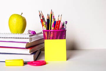 On a light background, textbooks, stationery, a sticker and an apple. School concept