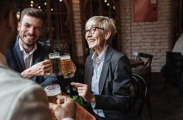 Senior businesswoman sitting with her younger male colleagues at cafe taking a brake and drinking beer.