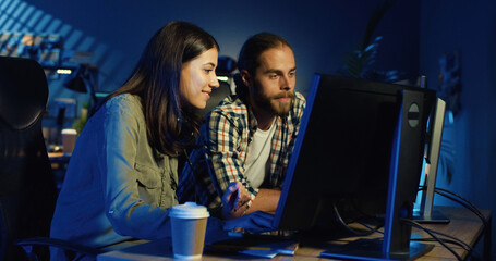 Picture of professional video editors editing video on computer with two displays in modern video studio. Young man and woman talking about project