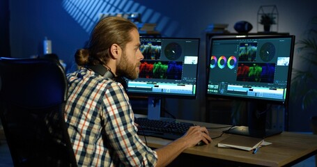 Portrait of professional video editor editing video on his personal computer with two displays in...