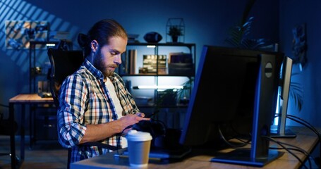 Portrait of professional video editor editing video on his personal computer with two displays in modern video studio. Young man works with headphones
