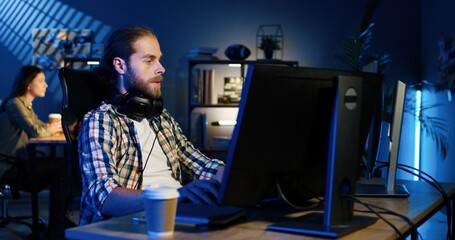 Picture of professional video editor editing video on his personal computer with two displays in modern video studio. Young man works with headphones