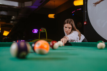 A beautiful caucasian girl in a white shirt is playing billiards