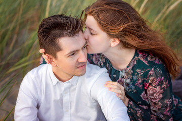 Fototapeta premium A young couple in love sitting on a background of green grass. The girl gently kisses her boyfriend on the forehead. Close up