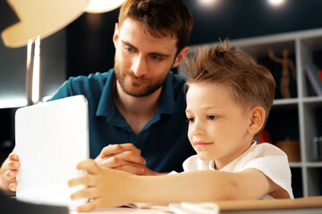 Young boy sitting with his father at the table and using laptop