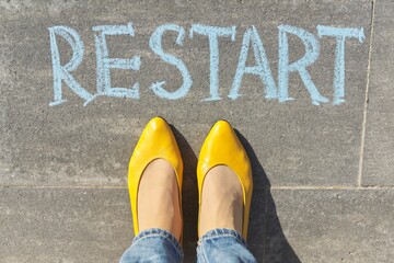 Restart concept, top view on woman legs and text written in chalk on gray sidewalk
