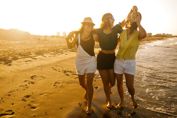 girlfriends walking on the beach a sunny summer day. They play with their hats, laugh and make jokes. There is a nice sunset