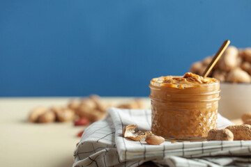 Closeup peanut butter in a glass jar, a handful of peanuts in shell. Foodphoto. Copy space. Breakfast for vegetarians.