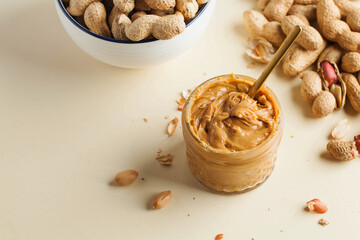 Closeup peanut butter in a glass jar, a handful of peanuts in shell. Foodphoto. Copy space. Breakfast for vegetarians.