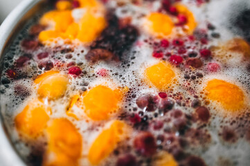 Fresh fruits: apricots, cherries, raspberries, apples are boiled in boiling water in a metal pan on a stove with bubbles and foam close-up. Cooking delicious homemade compote. Photography, concept.