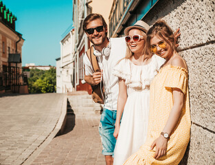 Fototapeta na wymiar Group of young three stylish friends posing in the street. Fashion man and two cute girls dressed in casual summer clothes. Smiling models having fun in sunglasses.Cheerful women and guy outdoors
