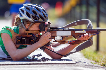 Young girl aiming rifle on biathlon shooting range