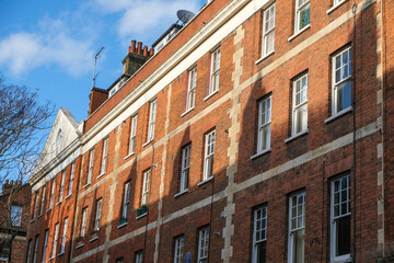 Fototapeta na wymiar A row of red brick buildings partly covered in shadows in London