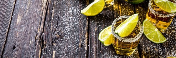 Golden tequila shots. Three tequila shot glasses with salt and lime slices, on wooden background copy space