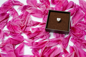 silver heart with text I love you in a jewellery box on pink peony petals